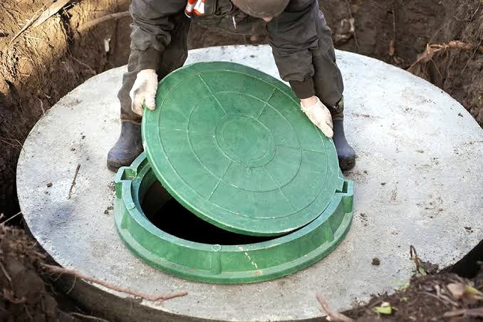 Worker opening green septic tank access lid